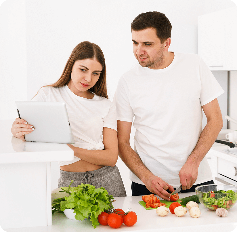 Couple using a tablet while preparing fresh vegetables in the kitchen, focusing on healthier nutrition decisions